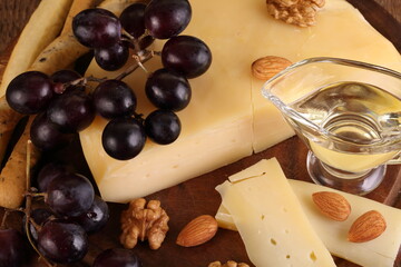Gruyere cheese on a wooden table with grapes, nuts and olive oil