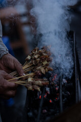 Bali, Indonesia - November 27, 2020: A Satay Maker Grilling Pork Satay in the Middle of a Cold Rainy Season in the Afternoon at Bedugul Village, Tebanan Regency, Bali, Indonesia on November 27, 2020