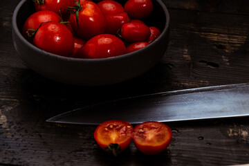 High angle shot of fresh red tomatoes on a bowl with knife and napkin on a wooden table