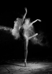 Obraz na płótnie Canvas A beautiful slender ballet dancer girl wearing a bodysuit and pointe shoes, posing dancing among the clouds of flying flour on a black background. Artistic, commercial, monochrome design
