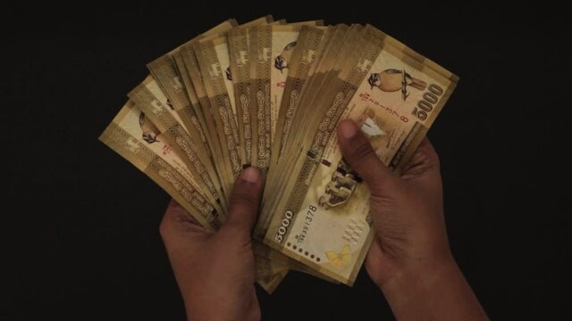 Counting money view from above, yellow 5000 rupee notes holding by the female hands, dark background.