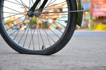 Rear wheel of bike which is flat and parked on the pavement beside the road.