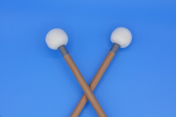Crossed timpani mallets on a blue background.
