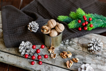 Obraz na płótnie Canvas Walnuts in a tin, whole and split, next to the filling and shell. Presented in a New Year's composition with cones, red berries and a sprig of a Christmas tree. Home storage of winter preparations