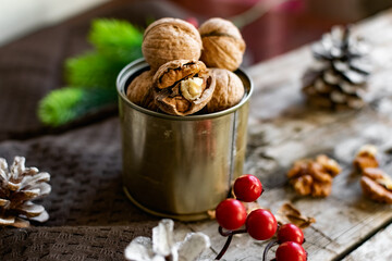 Walnuts in a tin, whole and split, next to the filling and shell. Presented in a New Year's composition with cones, red berries and a sprig of a Christmas tree. Home storage of winter preparations
