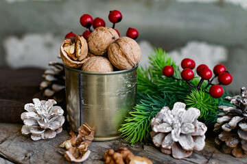 Obraz na płótnie Canvas Walnuts in a tin, whole and split, next to the filling and shell. Presented in a New Year's composition with cones, red berries and a sprig of a Christmas tree. Home storage of winter preparations