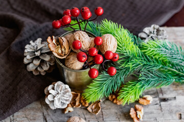 Walnuts in a tin, whole and split, next to the filling and shell. Presented in a New Year's composition with cones, red berries and a sprig of a Christmas tree. Home storage of winter preparations