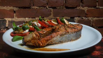 Caprese salad with cherry tomatoes, mozzarella toast and grilled salmon fish on the red brick wall...