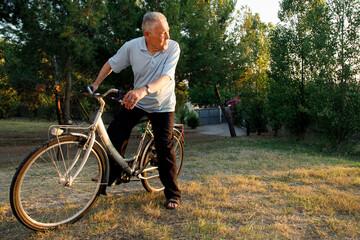 Obraz premium Signore ottantenne sta in sella alla sua bicicletta in un prato verde al tramonto
