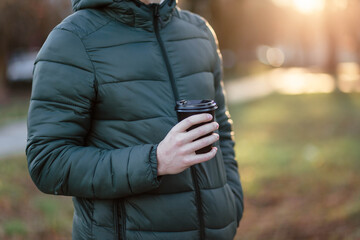 The guy holds a paper cup with coffee or tea. Have a cup of coffee. Disposable paper cup. Hot drink. Empty space. Man standing in the street holding a cup of coffee. Good morning.