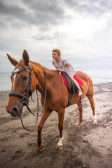 Pretty little girl riding horse on the beach. Happy childhood. Sunset time by the sea. Outdoor activities. Vacation concept. Bali, Indonesia