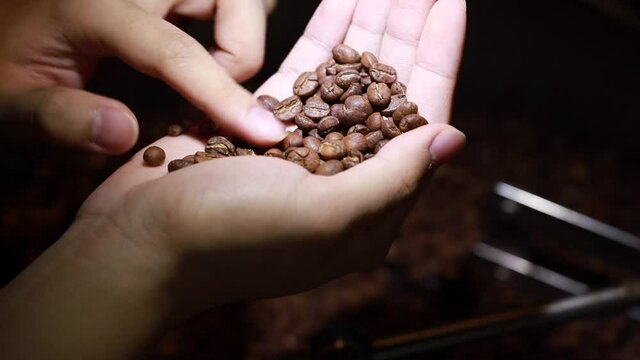 Close-up shot of Mixing dark roasted coffee beans in a cooler. Freshly roasted coffee beans on a cooling tray, being mixed by a rotating mechanical arm.