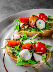 Italian bruschetta with roasted tomatoes, mozzarella cheese, balsamic vinegar and herbs on plate