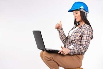 A woman architect in a hardhat, communicates via video on notebook, thumb up gesture, approval or agreement on white