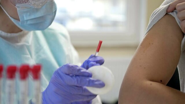 Nurse wearing goggles, a mask and disposable gloves injects the vaccine into the patient's shoulder. Mass vaccination begins. Stop the COVID-19 pandemic.