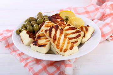 Roasted Halloumi with lemon and olives on white wooden table