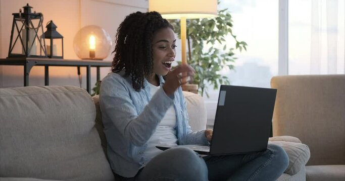 Astonished woman celebrating online success using laptop at home