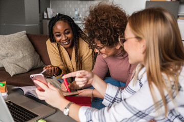 Group of multi ethnic female students learning at home using laptop and books for research.	