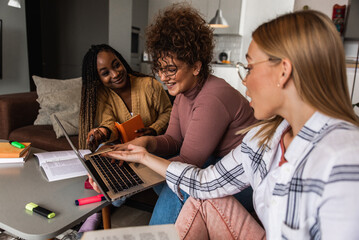 Group of multi ethnic female students learning at home using laptop and books for research.	