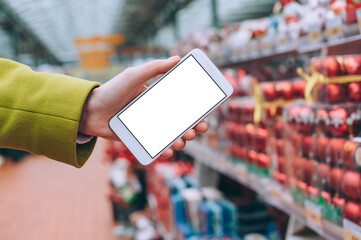 The girl holds a smartphone mockup in her hands. Against the background of the store. Concept for shopping for Christmas, New Year.
