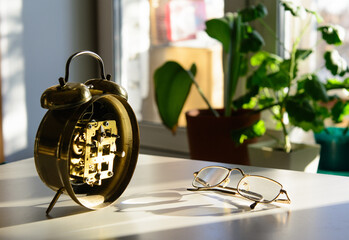 On the table is an alarm clock with the mechanism open in front of the window. Gold-rimmed glasses...