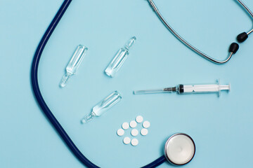 Close up of pills, ampoules, syringe and stethoscope on the blue background. Coronavirus, virus, flu or pneumonia.  