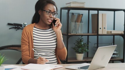 Young polite beautiful female manager sitting in office and answering customer calls. Work of consultant in office.