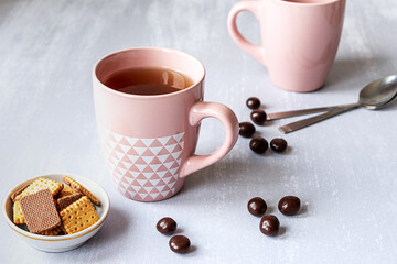 Pink cup of black tea on grey background, with cookies, chocolates and spoons. 