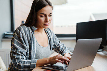 Charming focused woman working with laptop while sitting at table