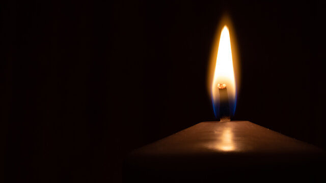 burning candle flame in the dark with copy space.  A lit candle on black background. The symbol of memory, hope and loss.
