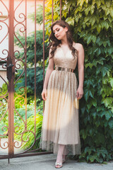 Beautiful teen girl in glamorous golden dress standing by the gate.