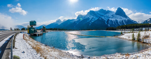 Rundle Forebay Reservoir in winter sunny day morning. Clear blue sky, snow capped Mount Lawrence Grassi mountain range in background. Canmore, AB, Canada. - obrazy, fototapety, plakaty