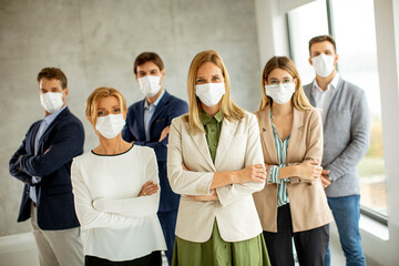 Business team members standing iwith protective facial masks and looking at the camera