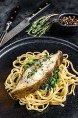 Baked Halibut fish steak and Spaghetti pasta with spinach. Black background. Top view