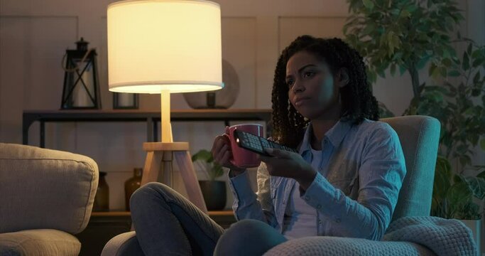 Bored african american woman changing channel and watching tv at night