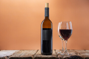 Bottle of red wine with empty glasses on rustic wooden table on beige background. Concept of alcoholic drink. Photo for advertising and product promotion. Space for text.