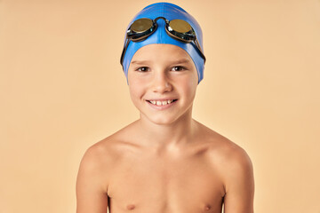 Cheerful boy swimmer standing against light orange background