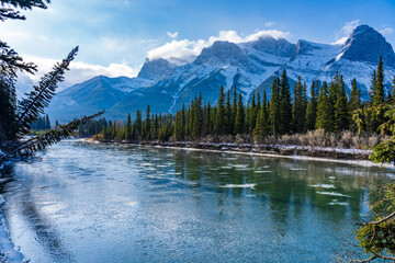 Natural scenery in early winter season sunny day morning. Drift ice floating on Bow River. Clear blue sky, snow capped Mount Lawrence Grassi in background. Landscape in Town Canmore, Alberta, Canada. © Shawn.ccf