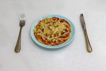 homemade pizza on a white background in a blue plate next to a fork and knife