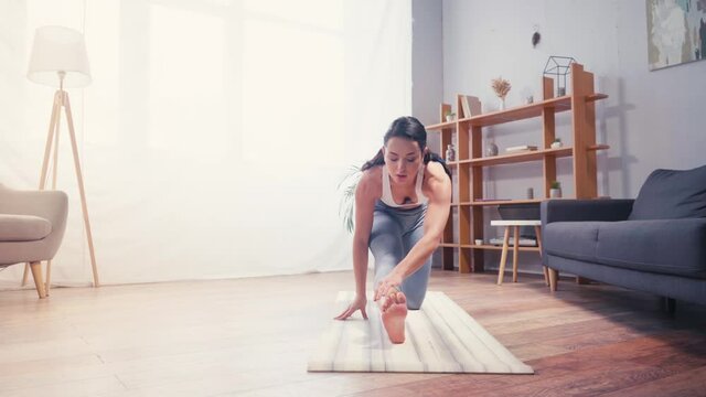 Young sportswoman stretching on fitness mat at home