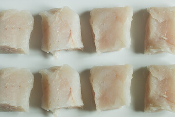 Pieces of raw hake in line on white ceramic texture background.