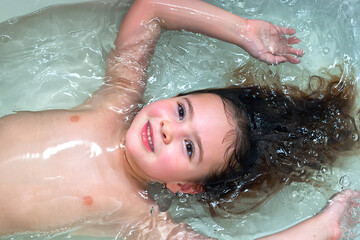 Happy little girl in the bath, swimming in the foam.