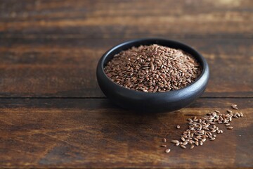 Flax seeds in a black ceramic bowl. Dark concrete background