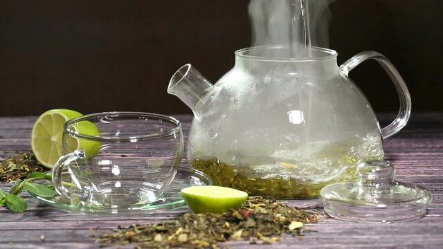 Green tea is poured into a glass cup from a glass teapot
