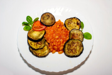 Fried eggplant on a plate with bean garnish.. Top view, white background