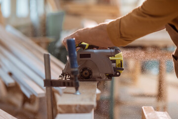 Carpenter sawing wooden bars with cordless electric saw at the joiner's workshop. Close-up with no...