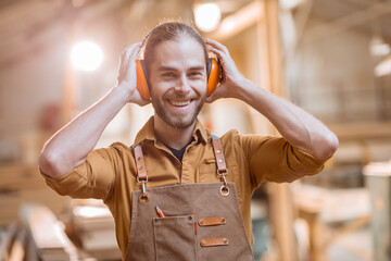 Portrait of a cheerful carpenter wearing headphones at the workshop