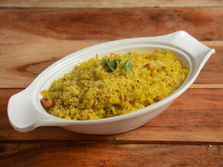 Poha, made with flattened rice, typically Western Indian breakfast, served in a plate over a rustic wooden background, selective focus