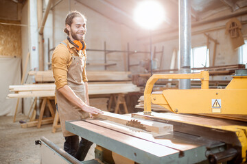 Carpentry worker sawing wooden planks with circular saw in the joinery warehouse