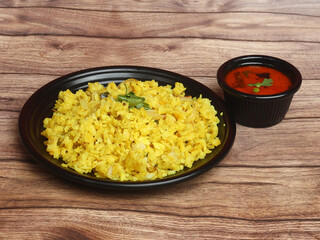 Poha, made with flattened rice, typically Western Indian breakfast, served with gravy over a rustic wooden background, selective focus